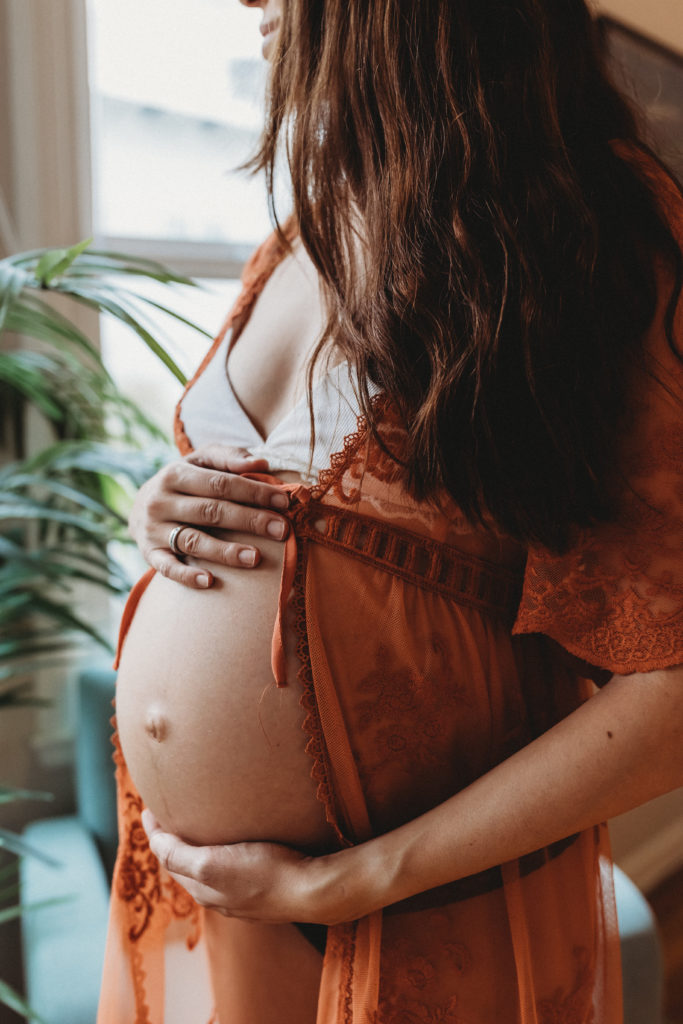 pregnant woman standing with hands on belly and looking out a window, intimate maternity photo, pregnancy photo