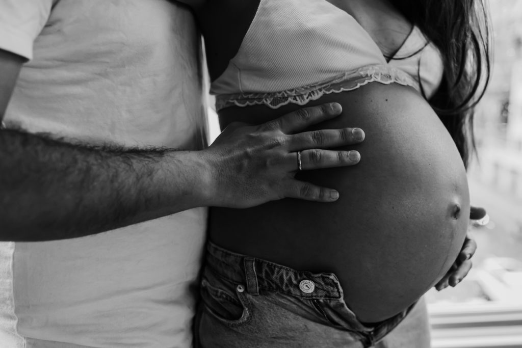 Close up of pregnant mother's belly with husband standing behind her with hand on her belly