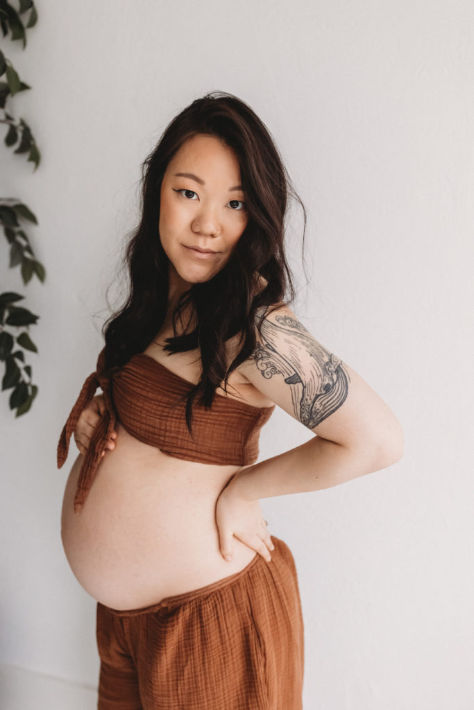 Pregnant woman standing with hands on her belly in a studio.