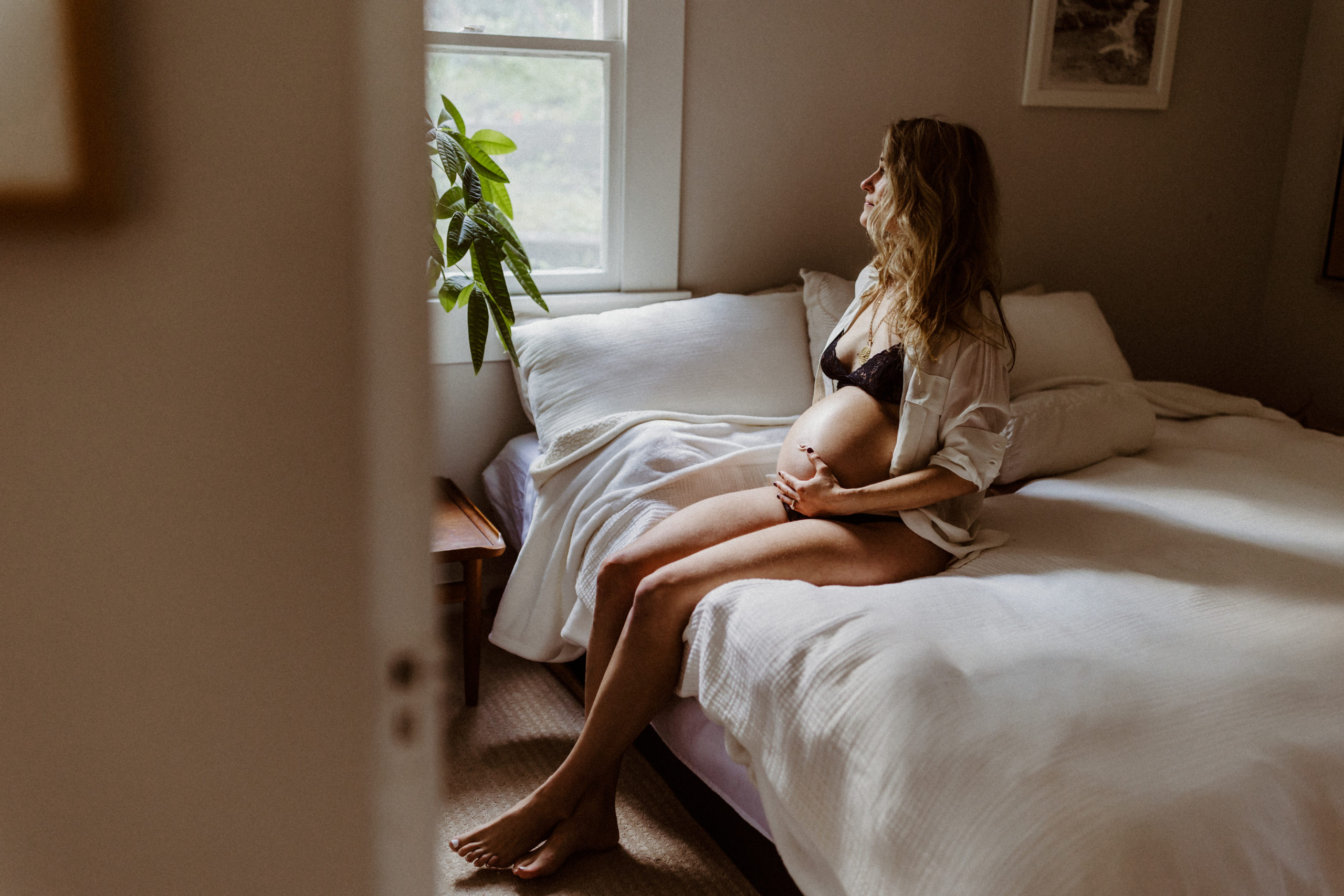 pregnant woman sitting on bed and looking out window, intimate maternity photo, pregnancy photo