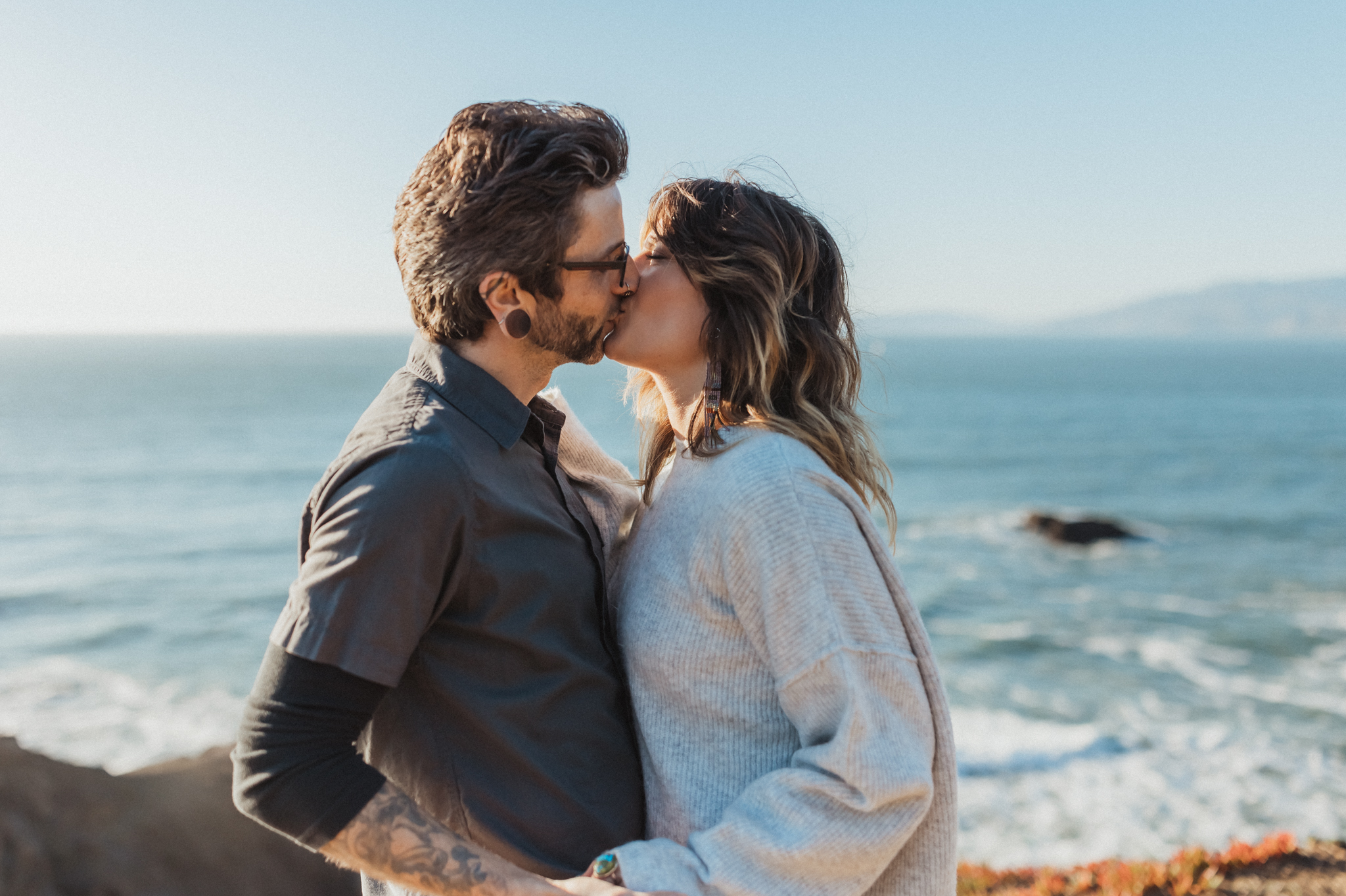 Man and woman kissing with the ocean behind them at the Sutro Baths in San Francisco during their outdoor engagement photo shoot.