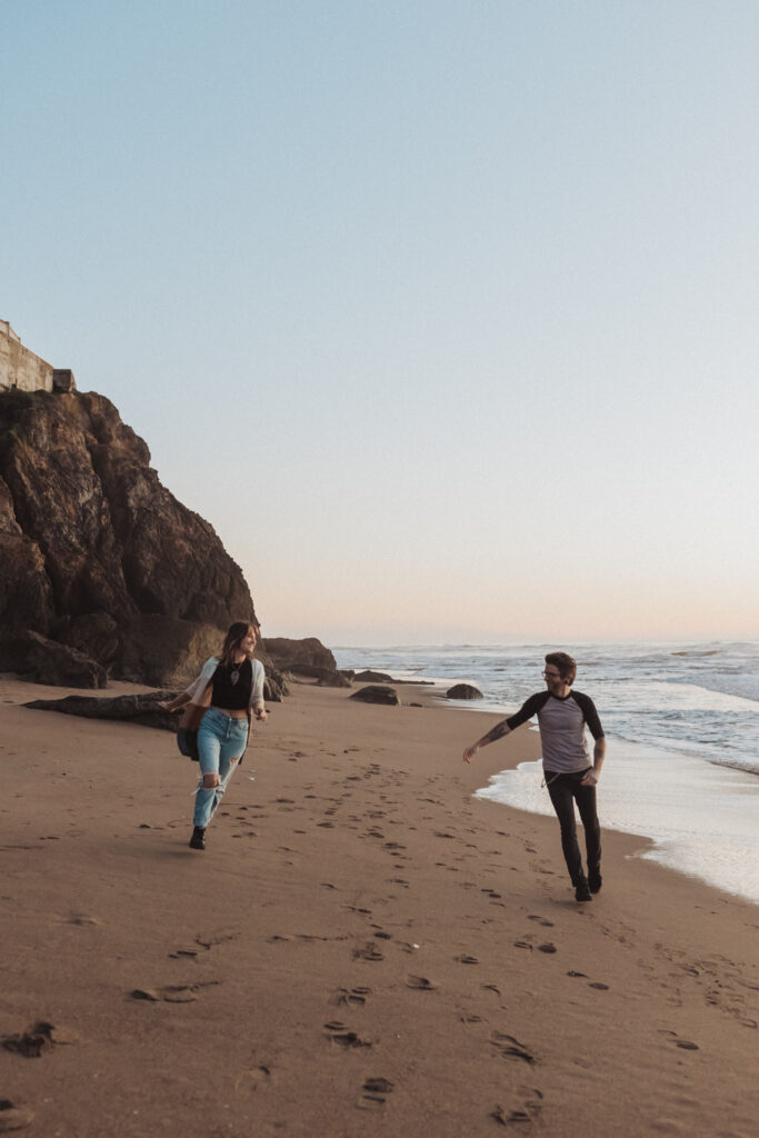 Couple running together on the beach at sunset at their engagement photo shoot at the Sutro Baths in San Francisco, California. - tips for feeling comfortable in front of the camera.