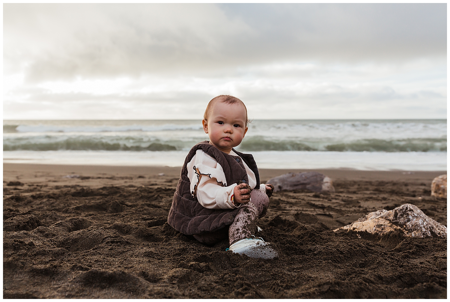 Happy baby covered in sand on the beach during a fun adventure family photo session.