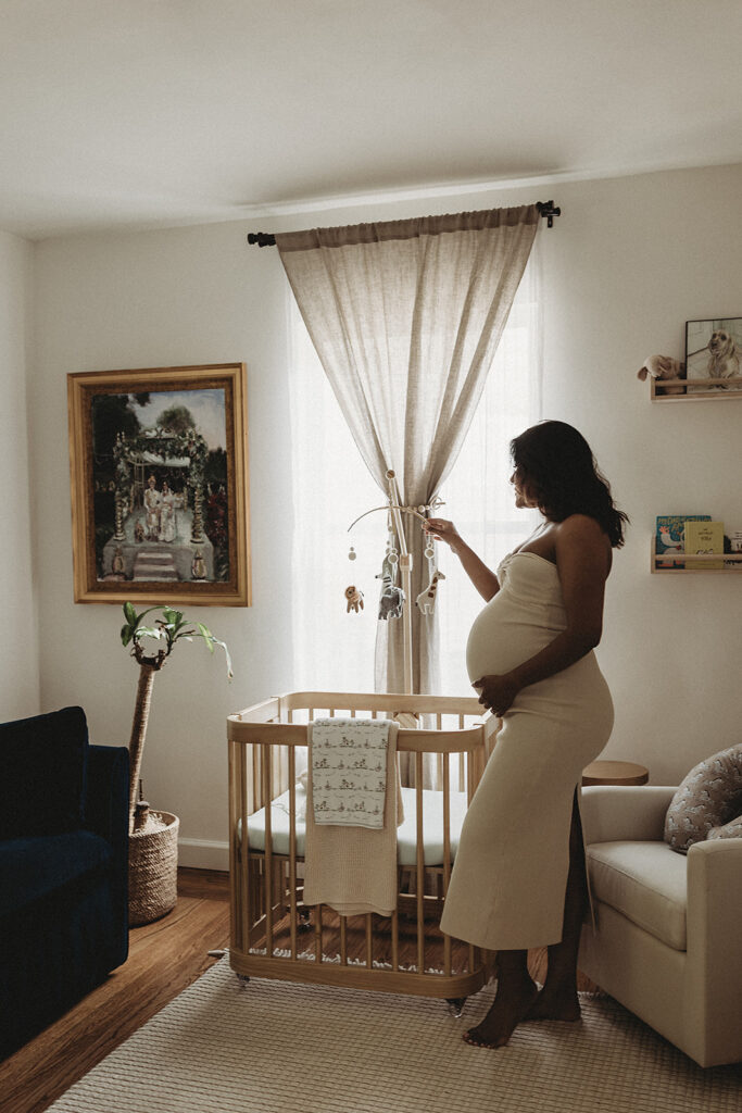 Pregnant mother admiring her baby's mobile hanging over the crib at home.