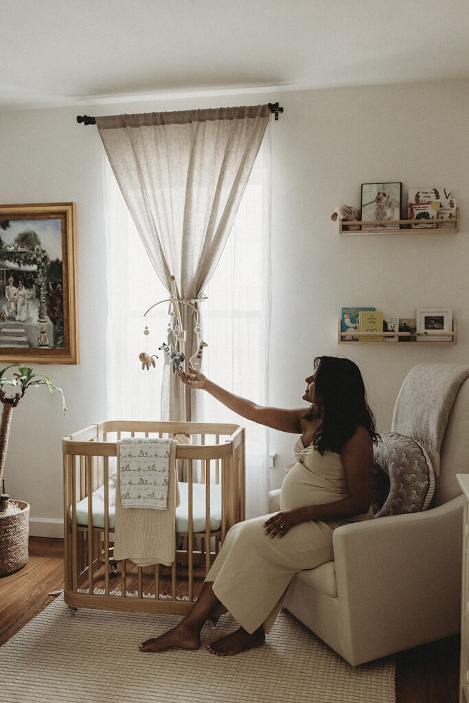 Pregnant mother admiring her baby's mobile hanging over the crib at home.