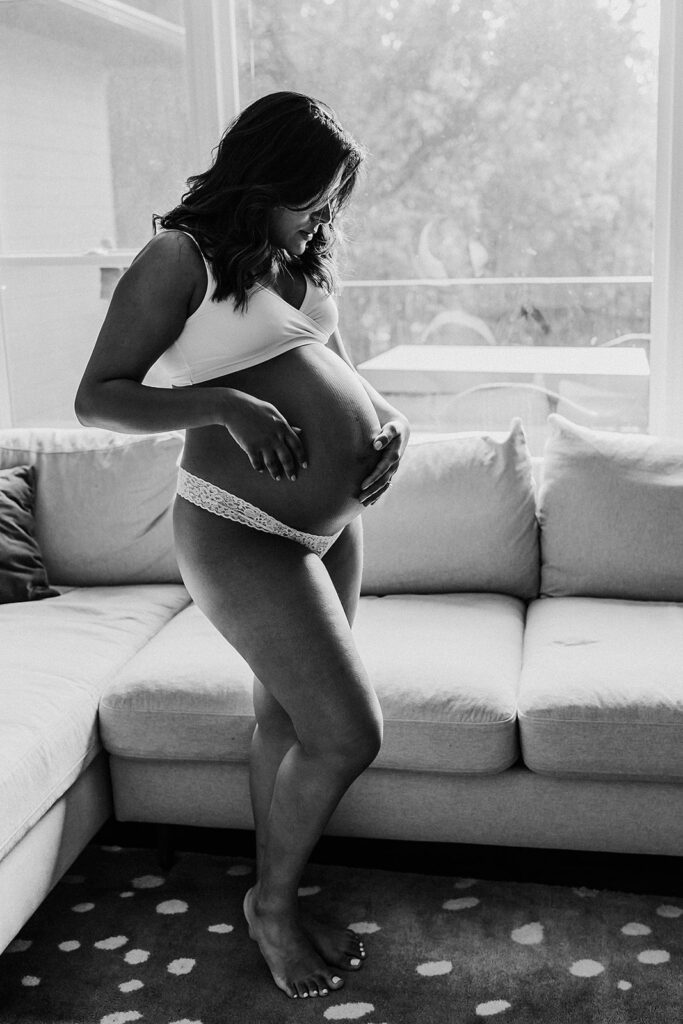 Pregnant woman looking down at belly in living room.