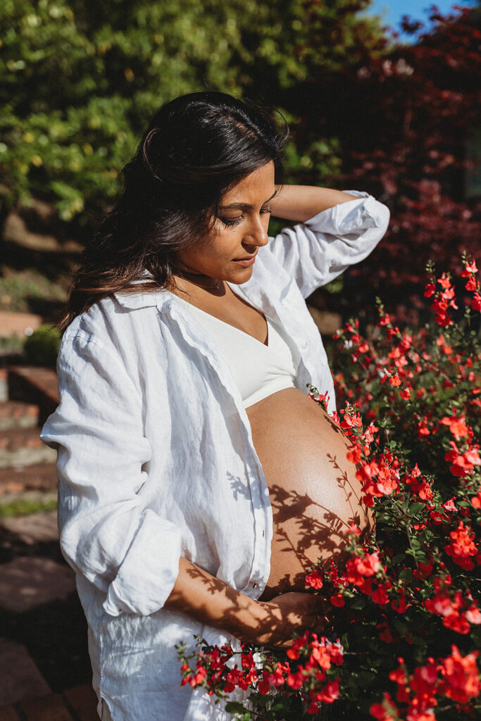 Pregnant woman outside with belly in blooming flowers.