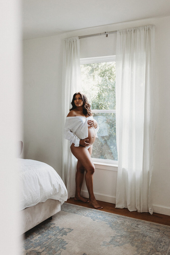 Pregnant mother standing by window in bedroom at home.