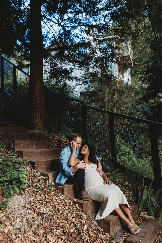 Expecting couple sitting on steps in a lush yard in Oakland.