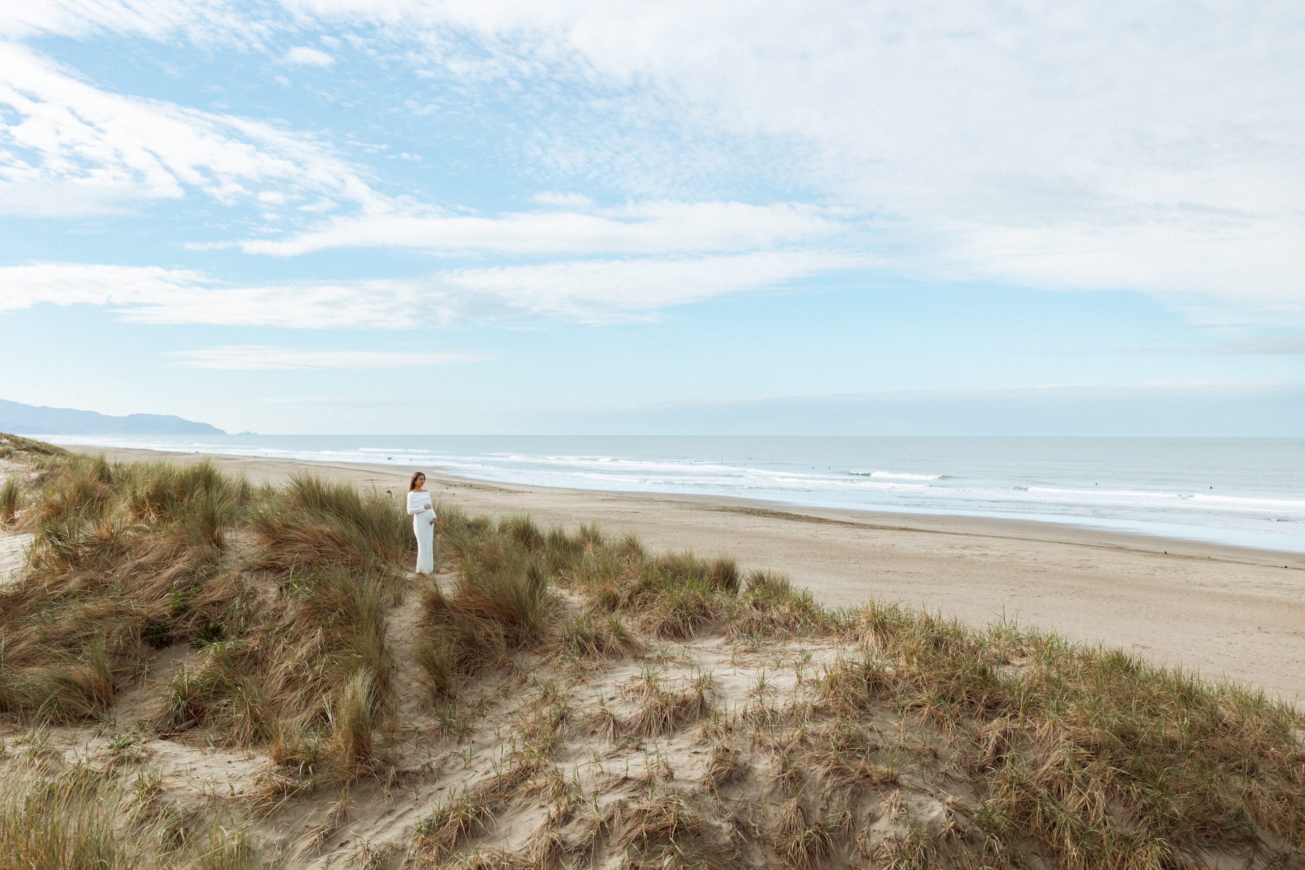 Pregnant mother standing on a sand dune at Ocean Beach in San Francisco and looking out at the ocean. Taken by Skyler Maire Photography.