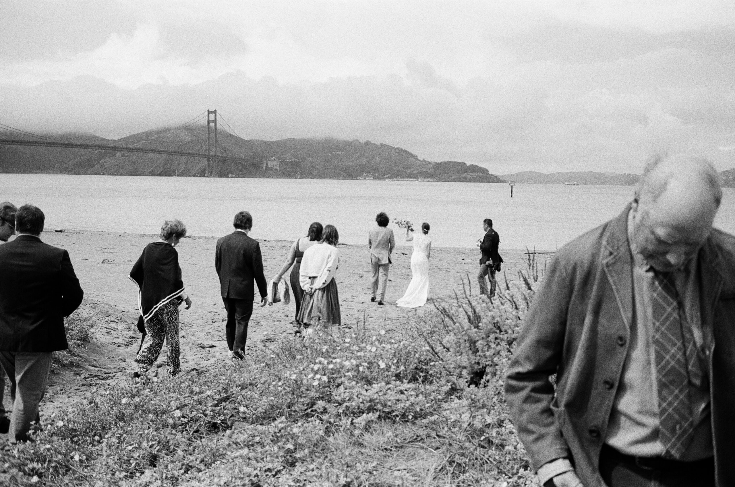 Newlywed couple and all their guests walking onto Crissy Field Beach in San Francisco after their intimate wedding ceremony.
