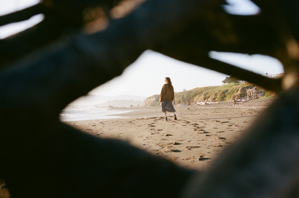 Creative photo of a girl standing on Moonstone Beach, taken through a wooden structure so there's a frame around the woman on the beach.