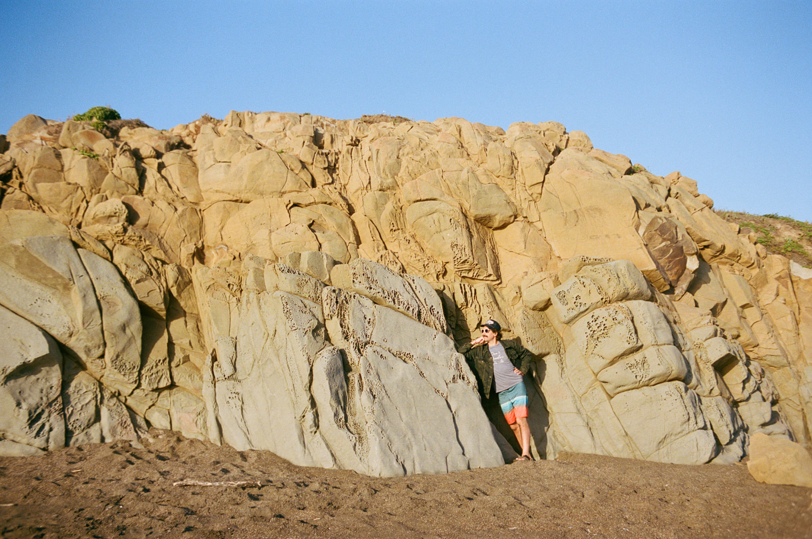Handsome man leaning against a rock wall at sunset on Moonstone Beach in Cambria, California.