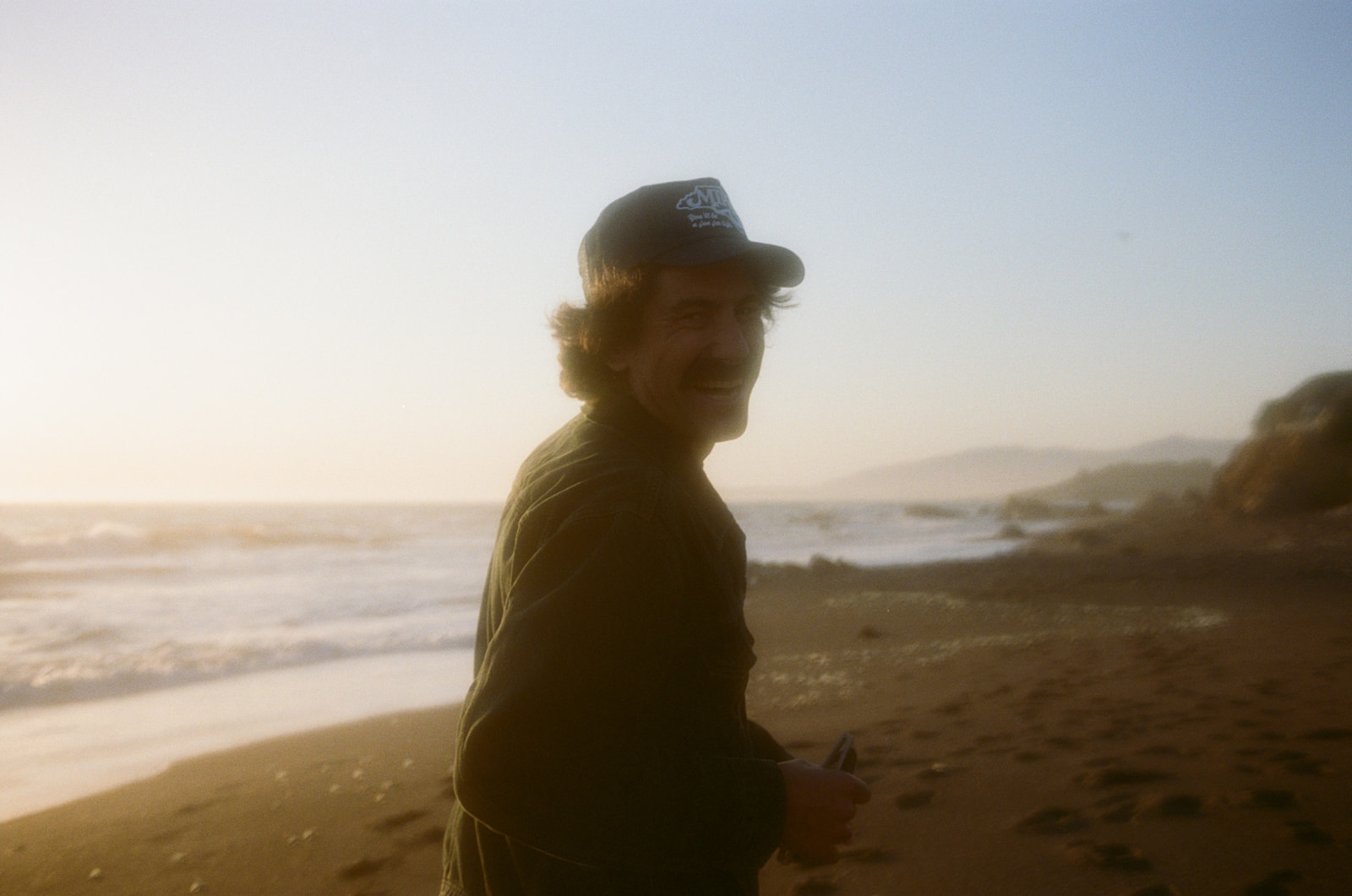 Hazy and playful image of a man laughing and looking back at the camera at sunset on Moonstone Beach in Cambria, California.