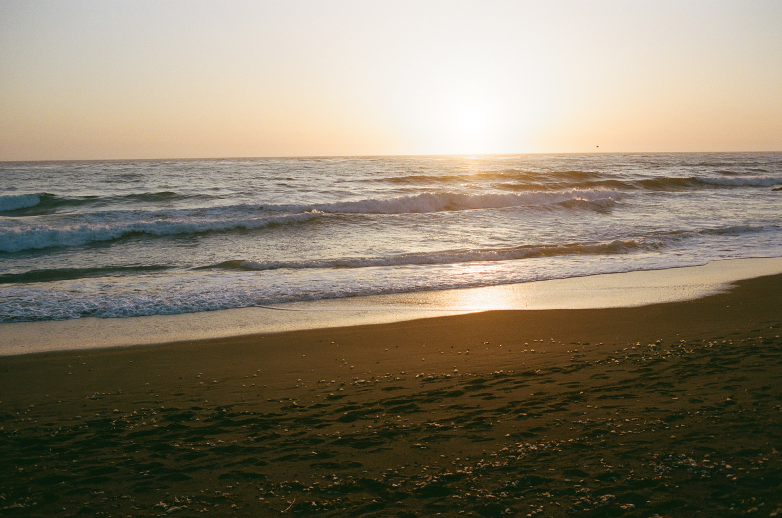The sun dipping behind the water at sunset on Moonstone Beach in Cambria, California. Taken by Skyler Maire Photography.